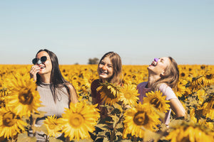 Three girls wearing colorful sunscreen on their noses while in a field of sunflowers